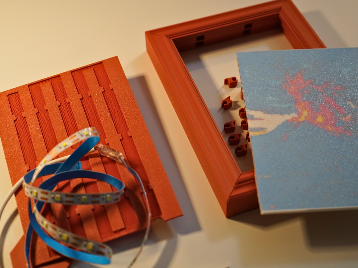 The parts of a lithophane frame laid out: channelled backer plate, LED strip, frame with prongs, and the lithophane pane