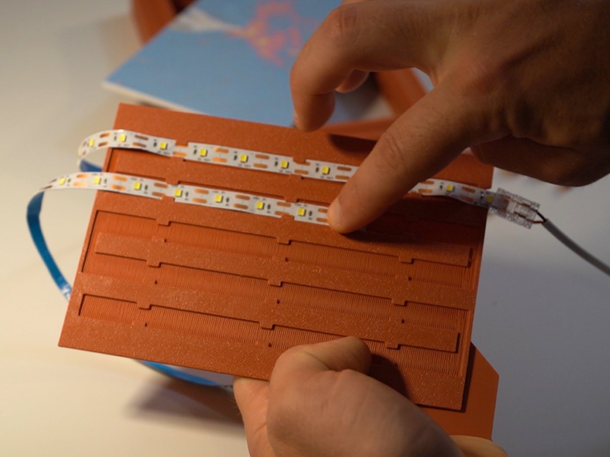 Hands pressing an LED strip into the routed channel of the printed backer plate